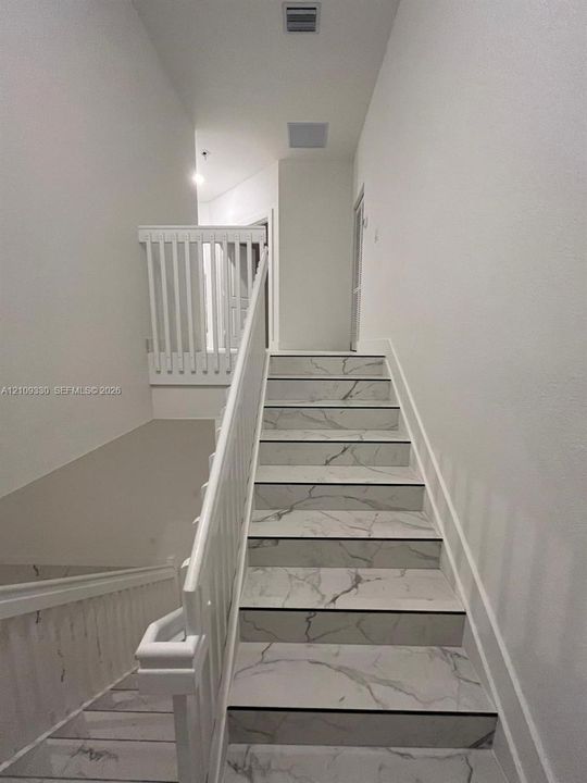 Staircase featuring white stone-patterned treads, white railing, and white balusters