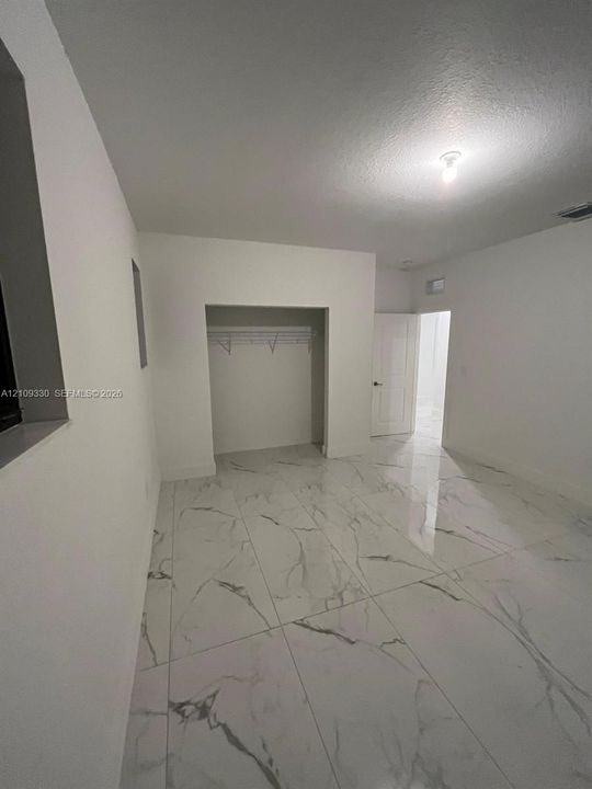 Neutral-toned room featuring large-format polished tile flooring with marble-style veining, recessed closet area, and crisp white wall finishes