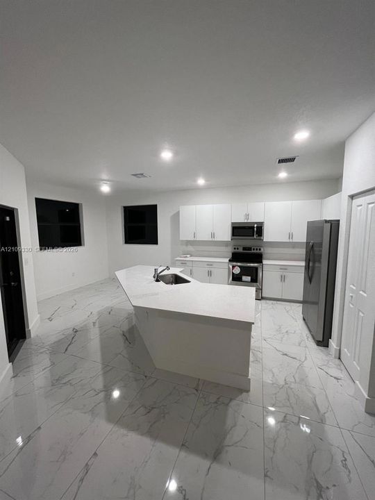 Kitchen featuring white cabinetry, quartz countertops, a central island with a stainless steel sink, large-format tile flooring, and stainless steel appliances