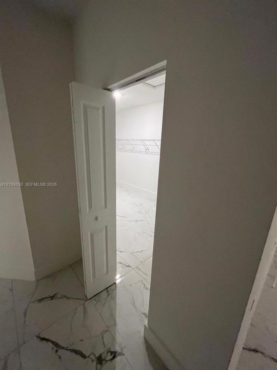 Storage space featuring white, six-panel bi-fold doors, white wire shelving, and large-format tile flooring with marble-pattern veining