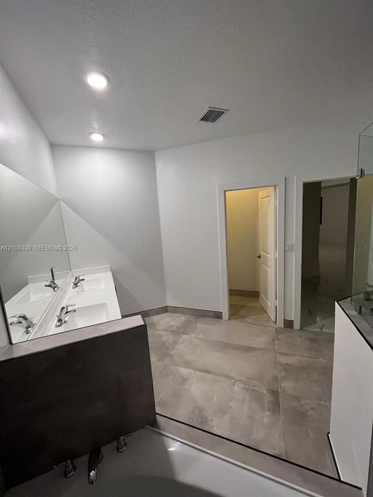 Dual-sink vanity with a large wall-mounted mirror, recessed ceiling lighting, and expansive floor tiling