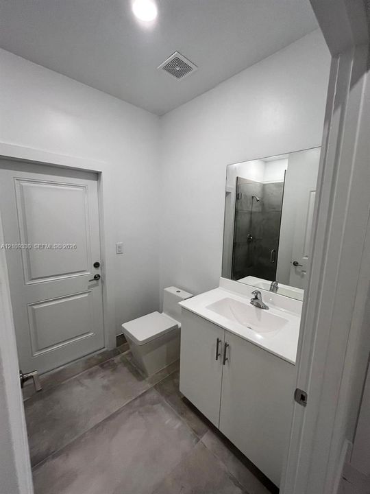 Bathroom featuring a white vanity cabinet with a integrated sink, polished chrome faucet, large frameless mirror, and neutral-toned tiled flooring