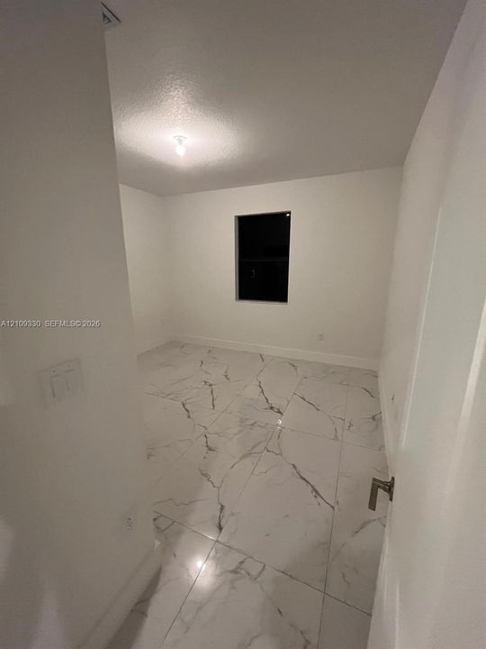 Interior space featuring large-format white stone-finish flooring with dark veining, neutral wall paint, and a single-pane window