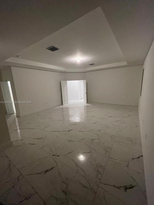 Tray ceiling, large-format stone-finish flooring with neutral veining, and double-door entry