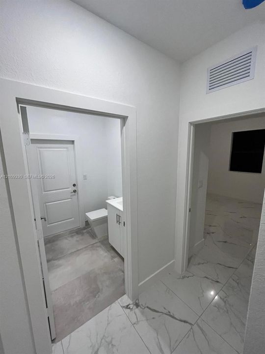 Large-format stone-style tile flooring with neutral veining, white shaker-style cabinetry, and solid-core interior doors