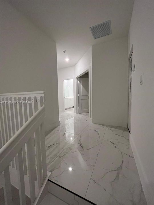 Large-format tile flooring with a veined pattern, white painted walls, and white wooden stair railing with vertical balusters