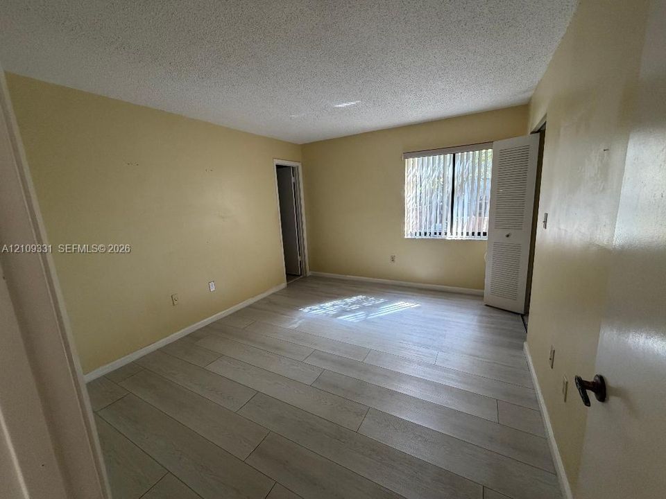 Interior space featuring wood-finish tile flooring, a window with vertical blinds, and a built-in closet with louvered doors