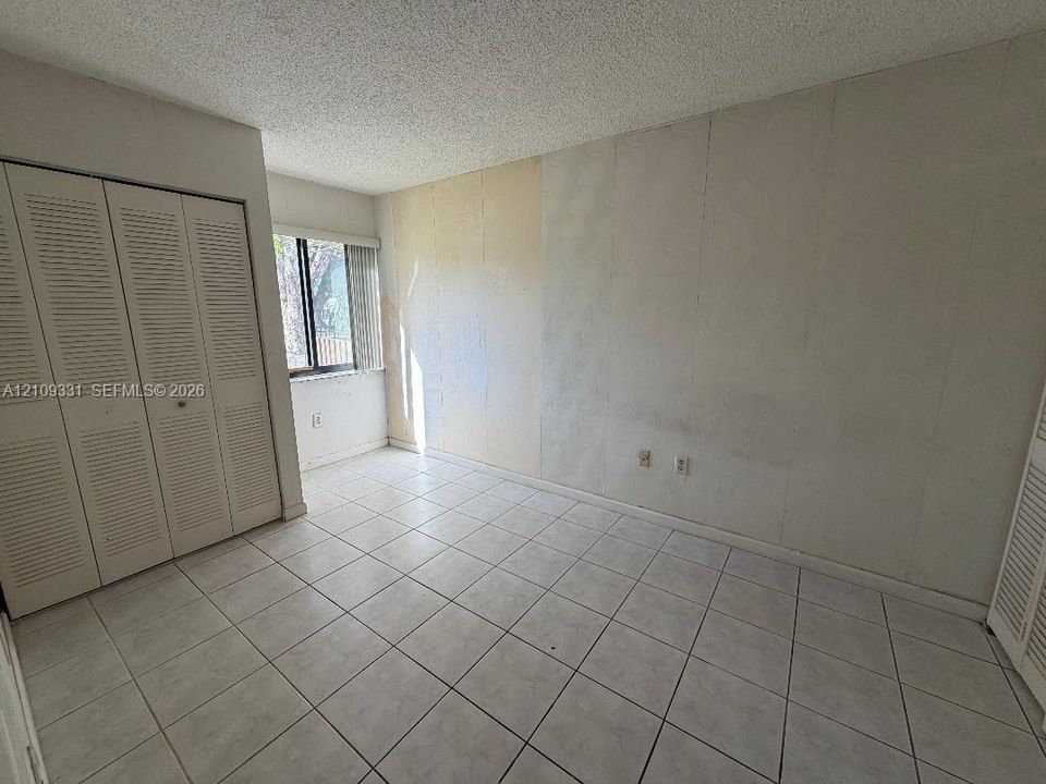 Room featuring white tile flooring, dual louvered-door closets, and a window with vertical blinds