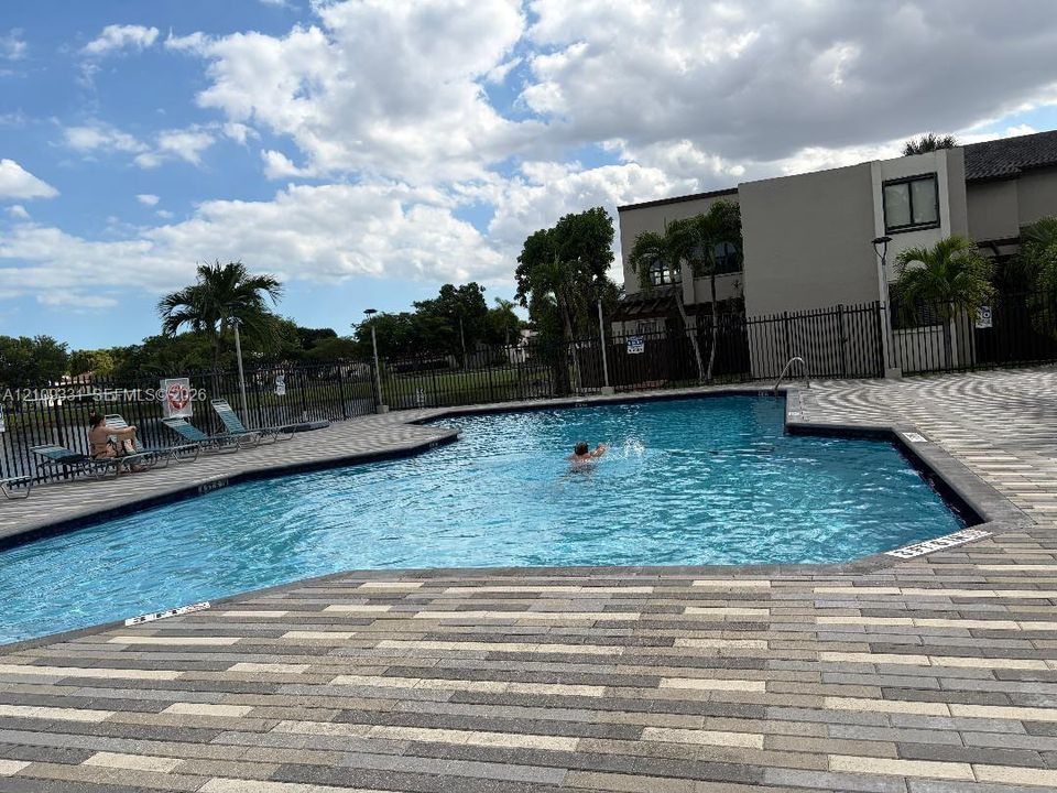 In-ground swimming pool featuring a multi-tone paver deck and metal perimeter fencing