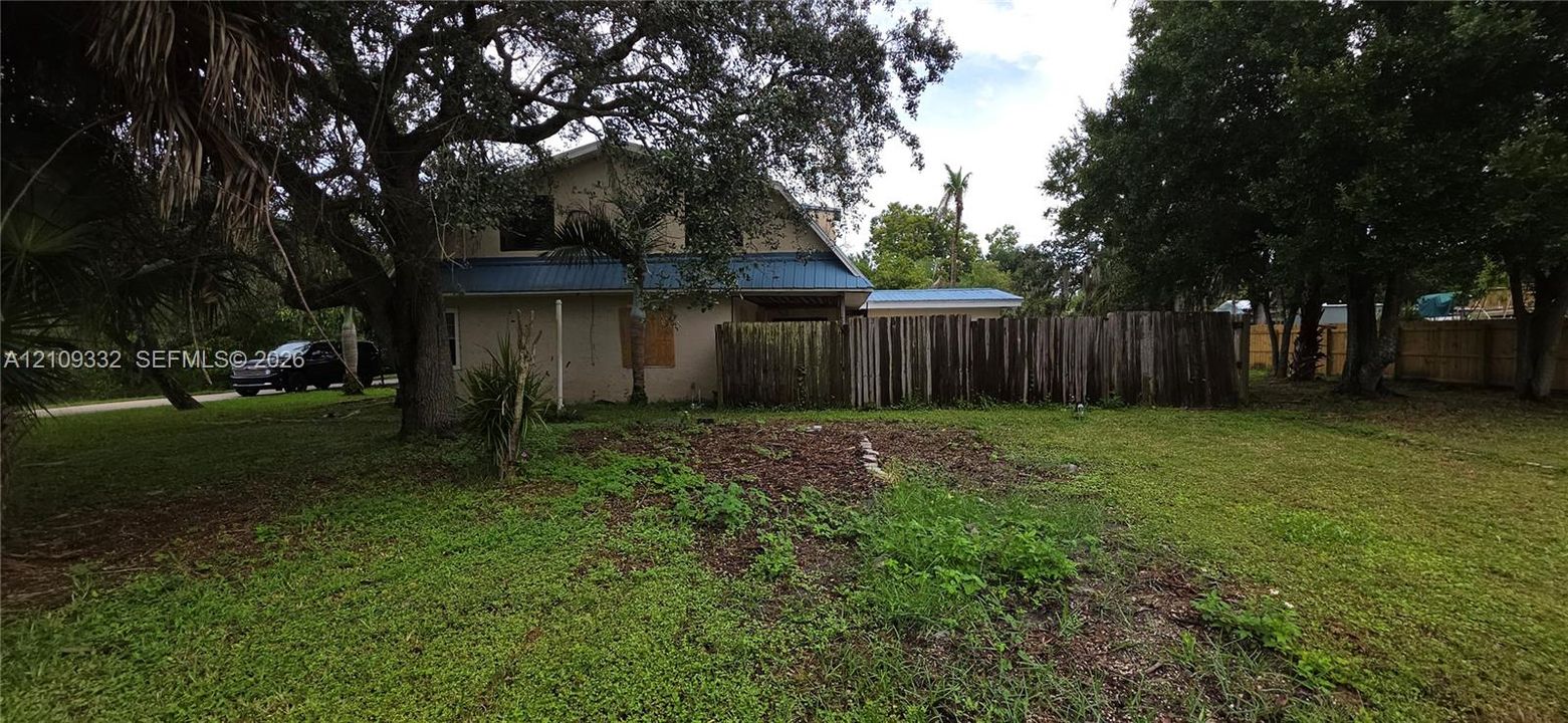 Exterior view featuring a multi-story residence with a blue metal roof, mature oak trees, and a wooden privacy fence