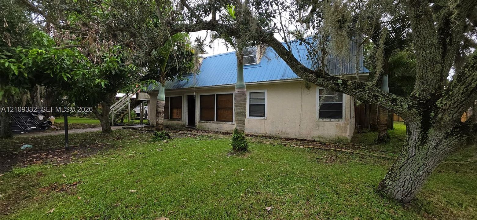 Stucco exterior residence featuring a blue metal roof, grass lawn, and mature canopy trees
