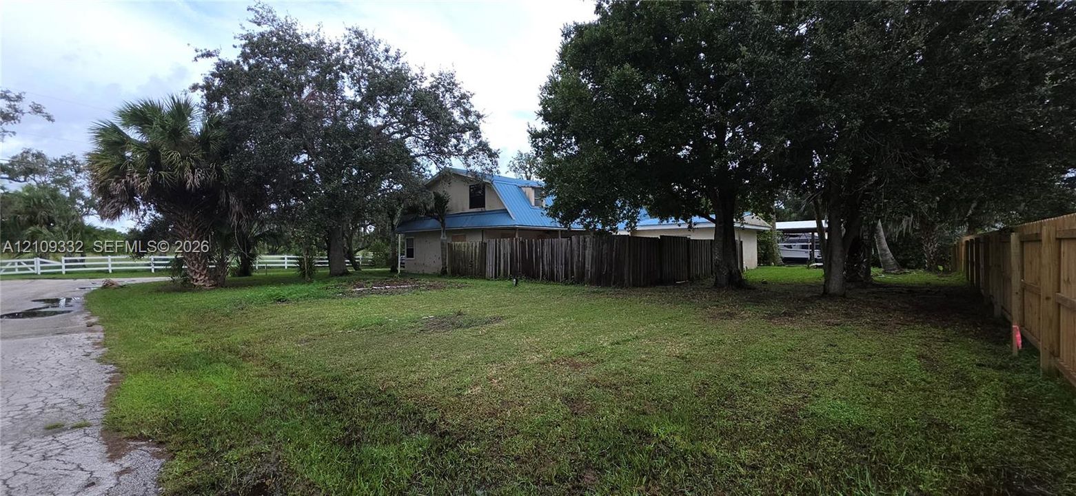 Expansive grounds featuring mature oak trees, established palms, wood fencing, and metal roofing
