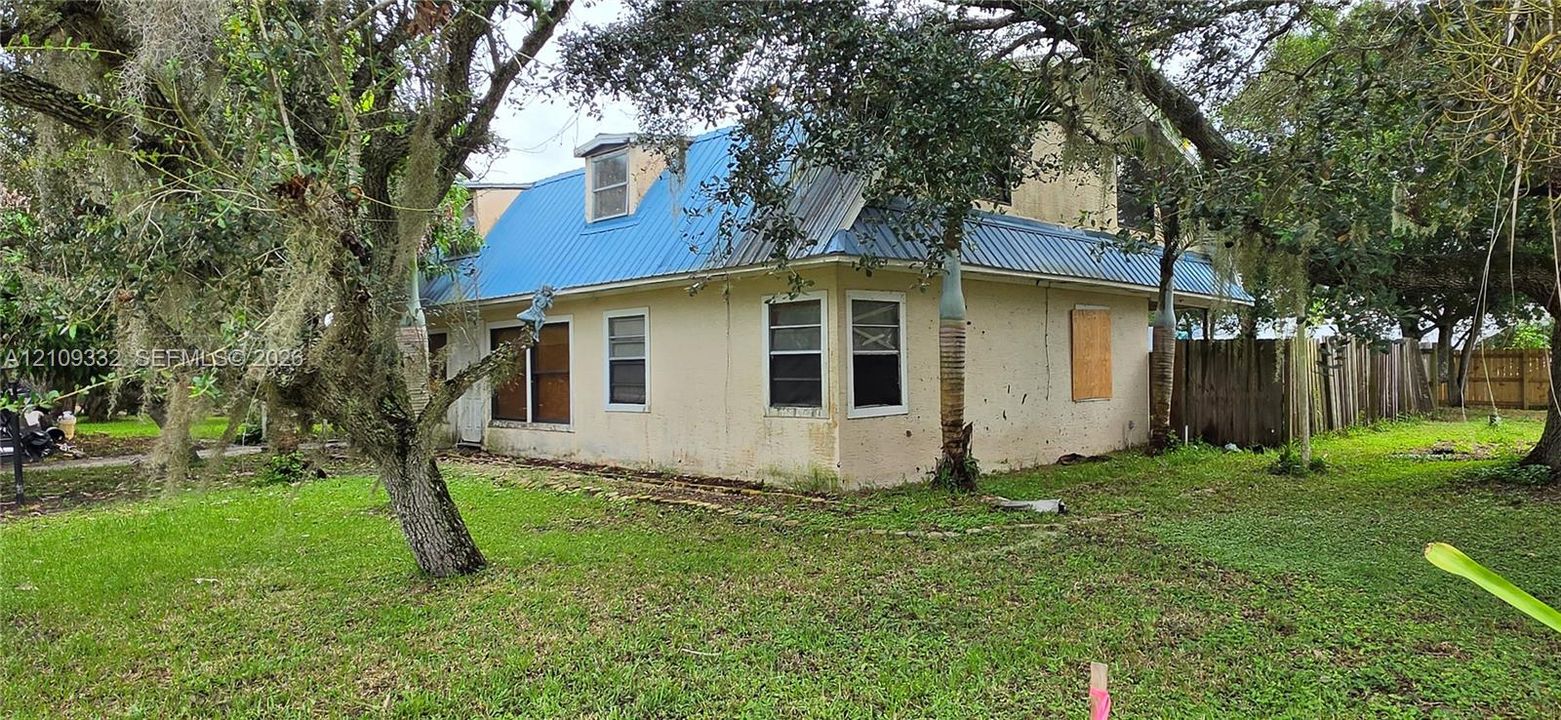 Stucco exterior residence featuring a blue metal roof, dormer windows, and a wood privacy fence