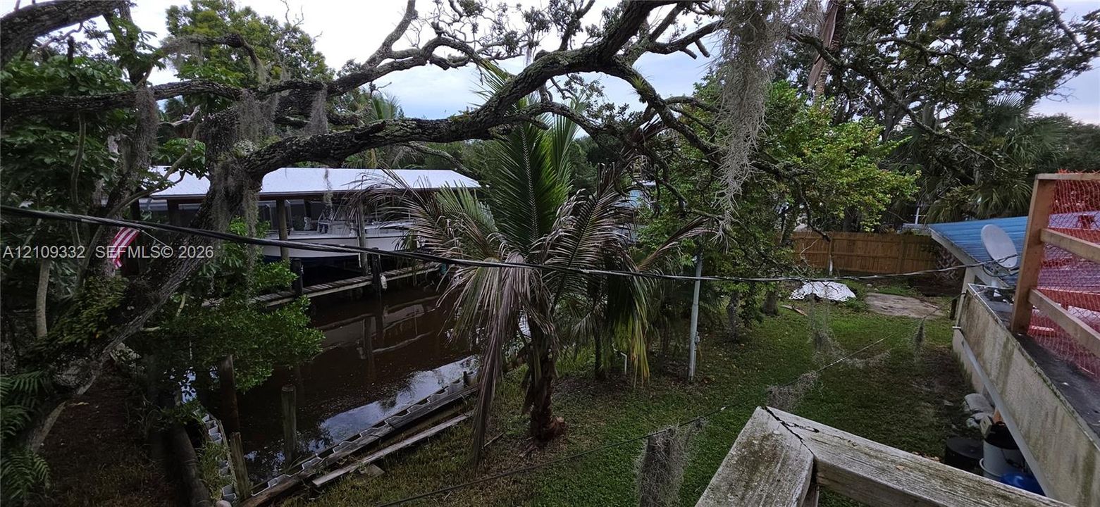 Canal-front property featuring a private boat dock, mature oak trees, tropical landscaping, and a fenced perimeter