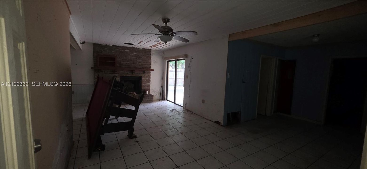 Interior space featuring tile flooring, a floor-to-ceiling brick fireplace with a wood mantel, a plank-style ceiling with an integrated fan, and a sliding glass door