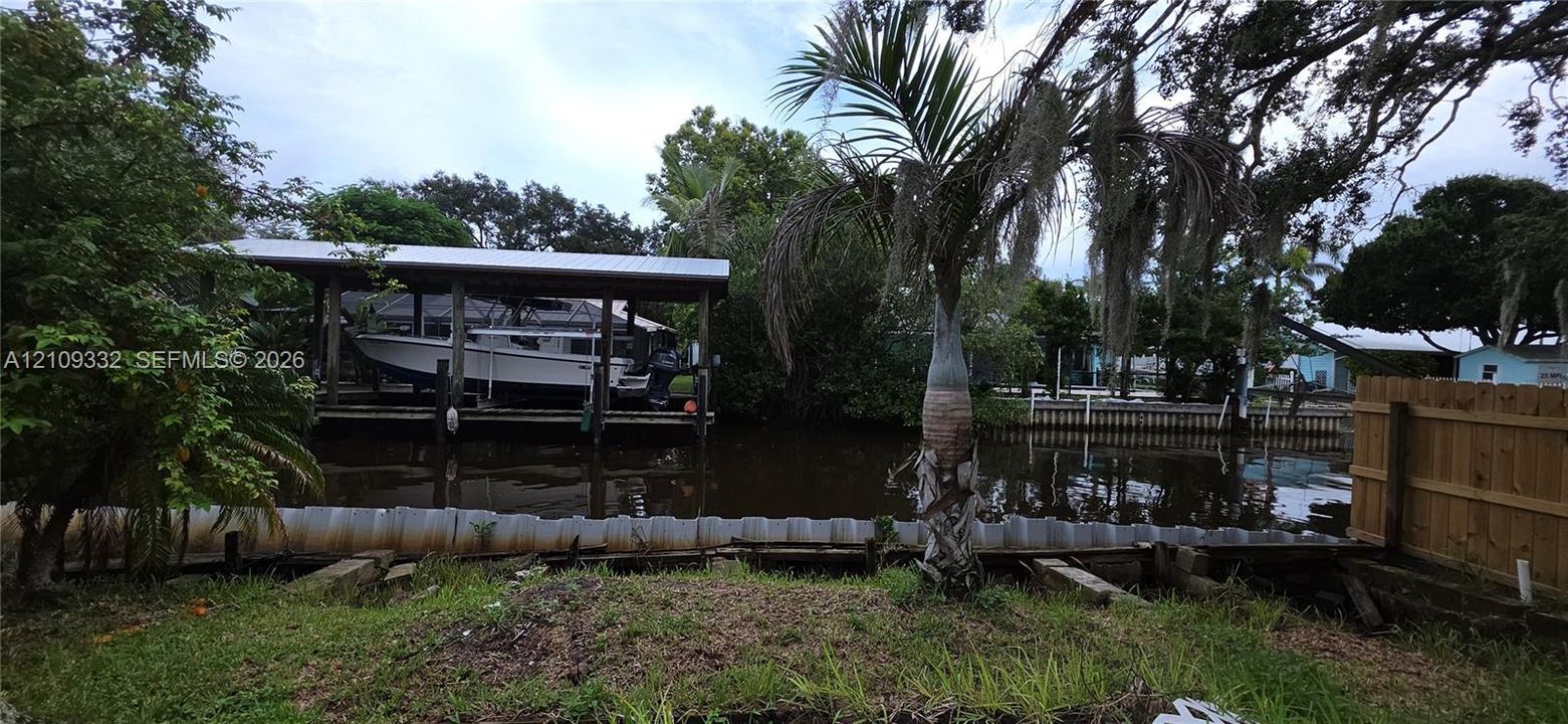 Waterfront property featuring a private covered boat lift, bulkhead seawall, and mature tropical landscaping