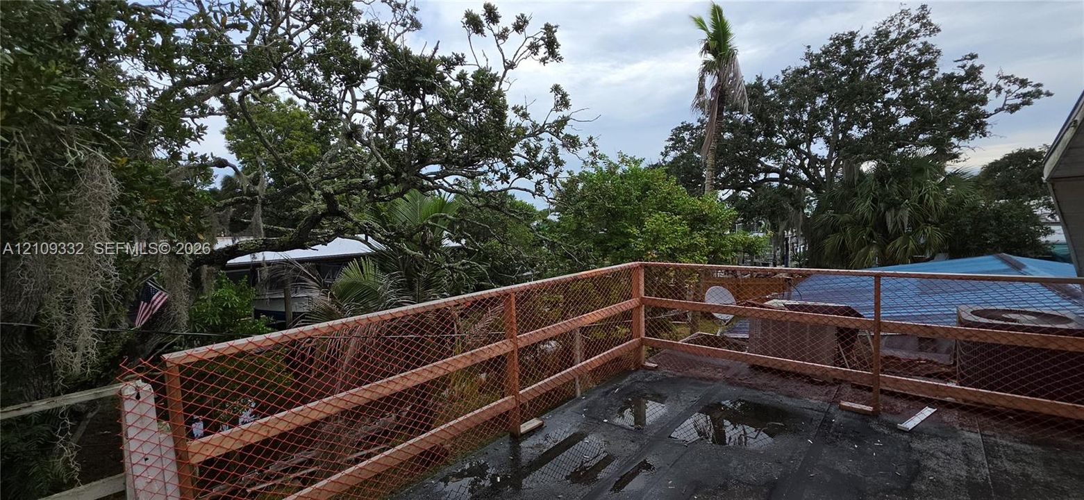 Elevated wooden deck featuring metal mesh railing and surrounding mature trees