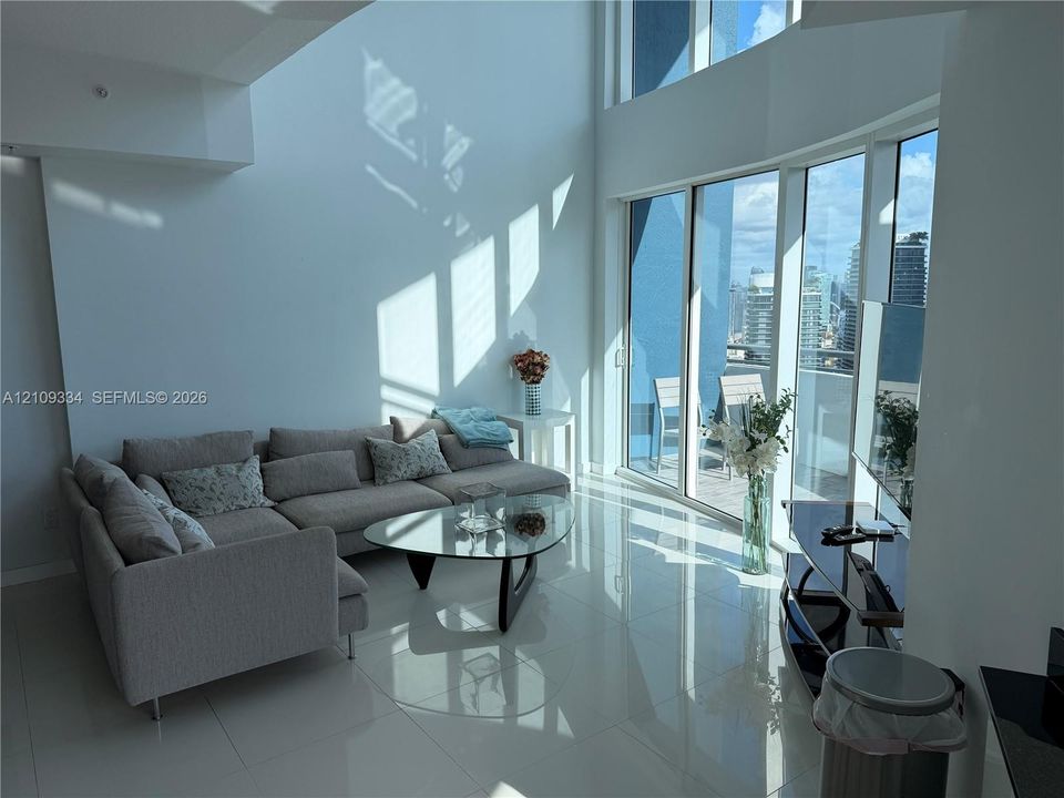 Double-height ceilings, floor-to-ceiling glass windows, polished tile flooring, and a private balcony