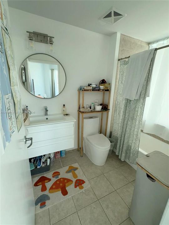Wall-mounted floating vanity with integrated rectangular sink and polished chrome faucet, circular mirror, modern wall-mounted lighting fixture, and ceramic tile flooring