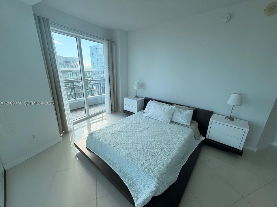 Floor-to-ceiling glass sliding door with access to a private balcony and large-format tile flooring throughout