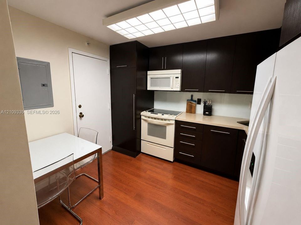 Kitchen featuring dark-finish cabinetry, solid-surface countertops, wood-finish flooring, integrated refrigeration, and a flush-mount grid ceiling light