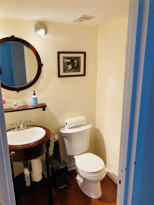 Console-style wood vanity featuring an integrated round mirror, porcelain basin, polished metal hardware, and wood-finish flooring
