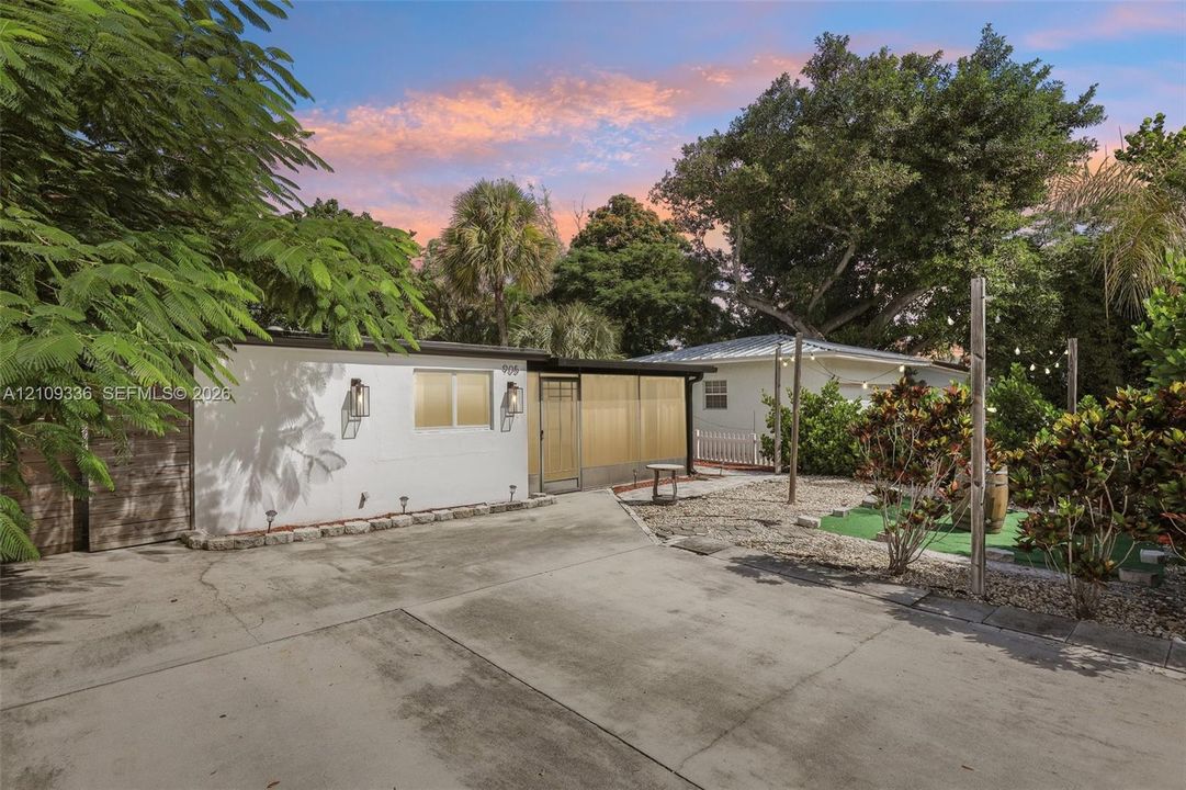 Exterior featuring a concrete driveway, metal-framed screened entryway, wall-mounted exterior lighting, and gravel landscaping