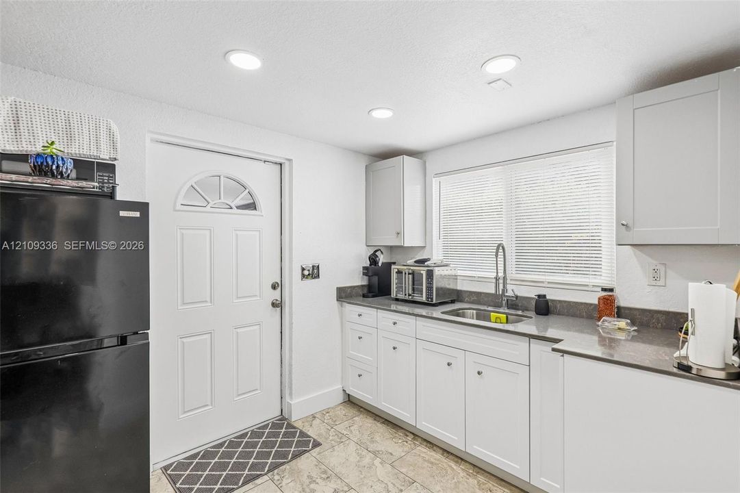 Kitchen featuring white Shaker-style cabinetry, dark stone-finish countertops, stainless steel undermount sink with arched pull-down faucet, tile flooring, and recessed ceiling lighting