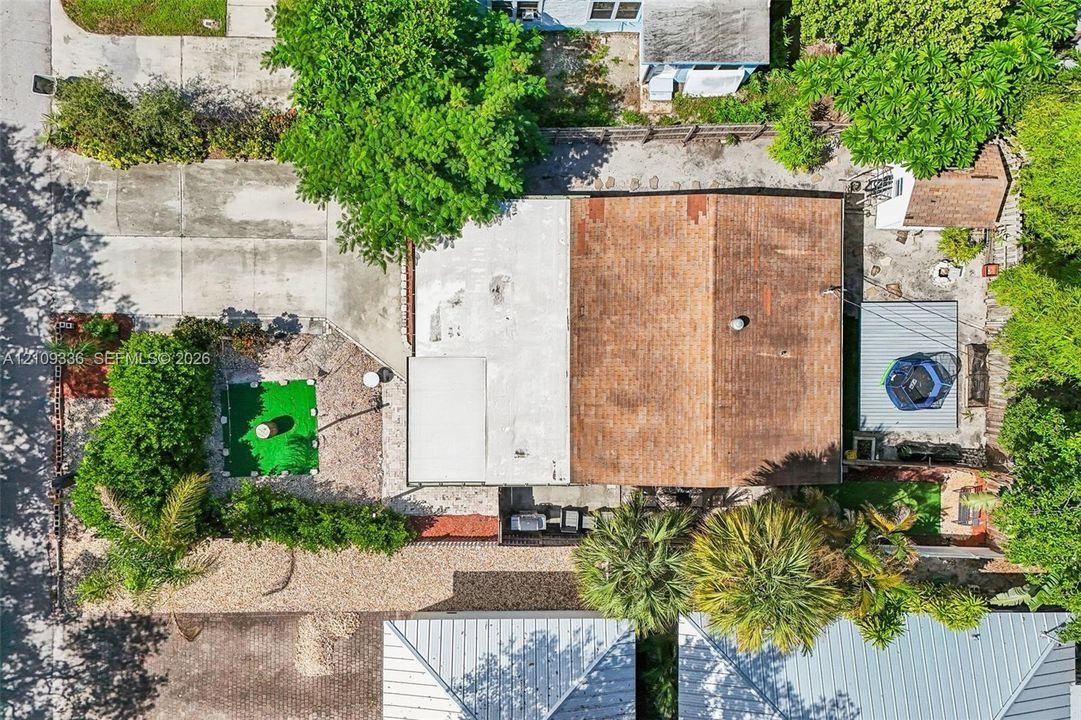 Aerial view of property featuring a multi-section roofline, expansive concrete driveway, stone-covered grounds, and mature landscaping