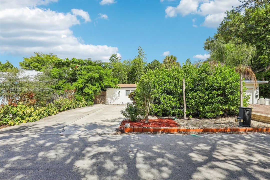 Concrete driveway, mature landscaping, and red mulch garden beds