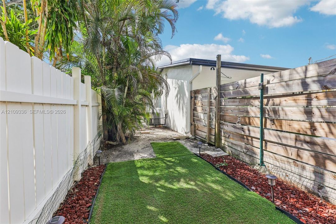 Side yard featuring white vinyl fencing, horizontal wood slat privacy fencing, artificial turf, and red decorative stone border