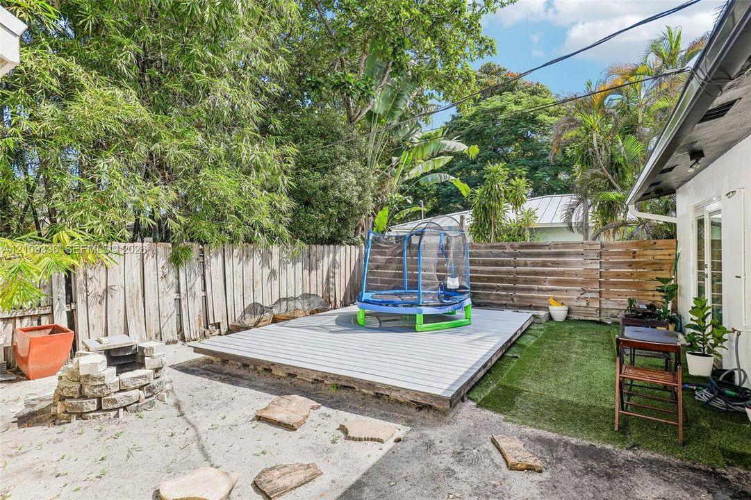 Rear exterior space featuring a raised composite deck, stone fire pit, horizontal wood fencing, and synthetic grass lawn