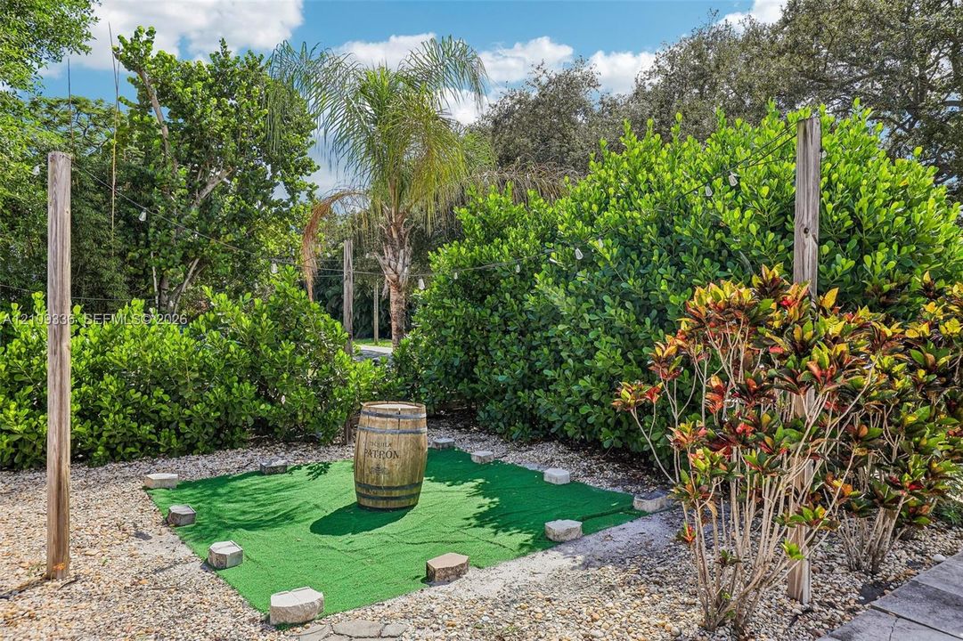 Outdoor area featuring synthetic turf, decorative stone border, perimeter string lighting, and mature tropical landscaping