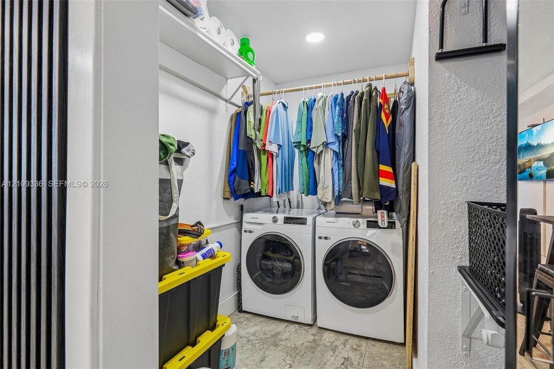 Laundry area featuring white front-loading washer and dryer, integrated overhead shelving, a dedicated garment rod, and tile flooring