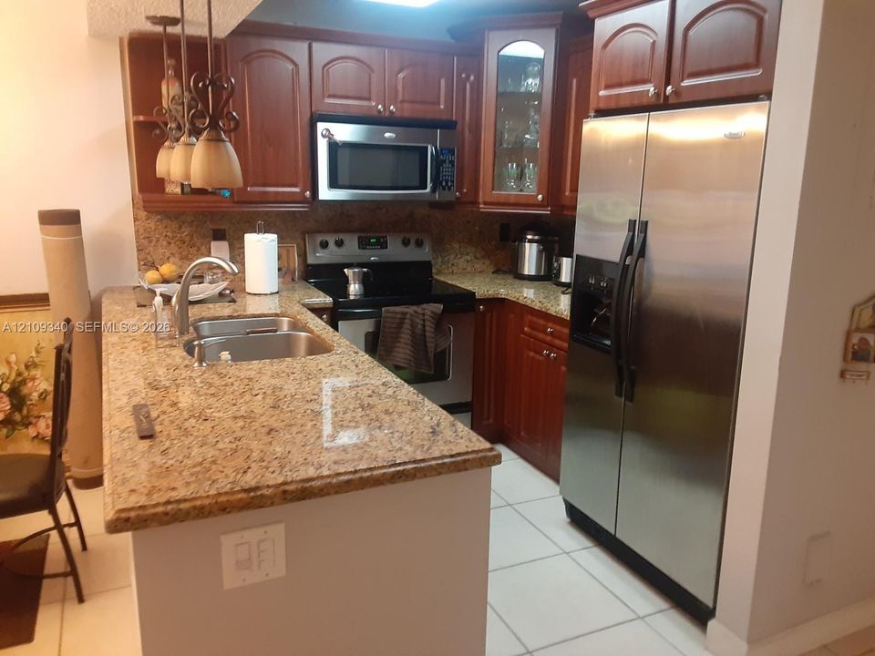 Kitchen featuring wood cabinetry, stone countertops, stainless steel appliances, a dual-basin undermount sink, and glass-front upper cabinet detailing