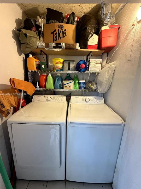 Utility space featuring a top-loading washing machine, clothes dryer, and tiered wire shelving