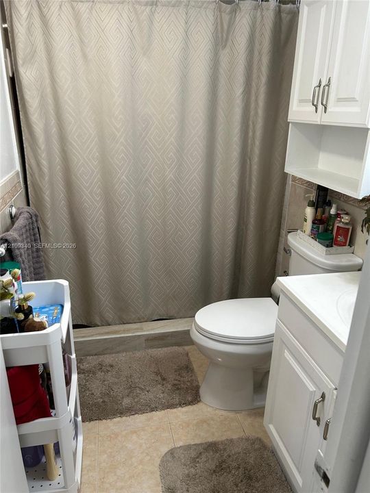 Bathroom featuring a tub-shower combination with tiled surround, white vanity cabinet, matching wall-mounted storage cabinetry, and hard-surface flooring