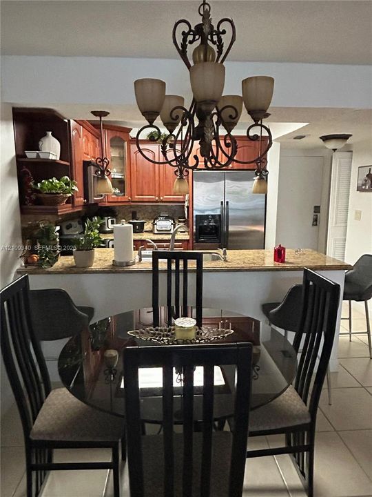Kitchen featuring wood cabinetry, stone-finish countertops, stainless steel refrigerator, and decorative wrought-iron chandelier