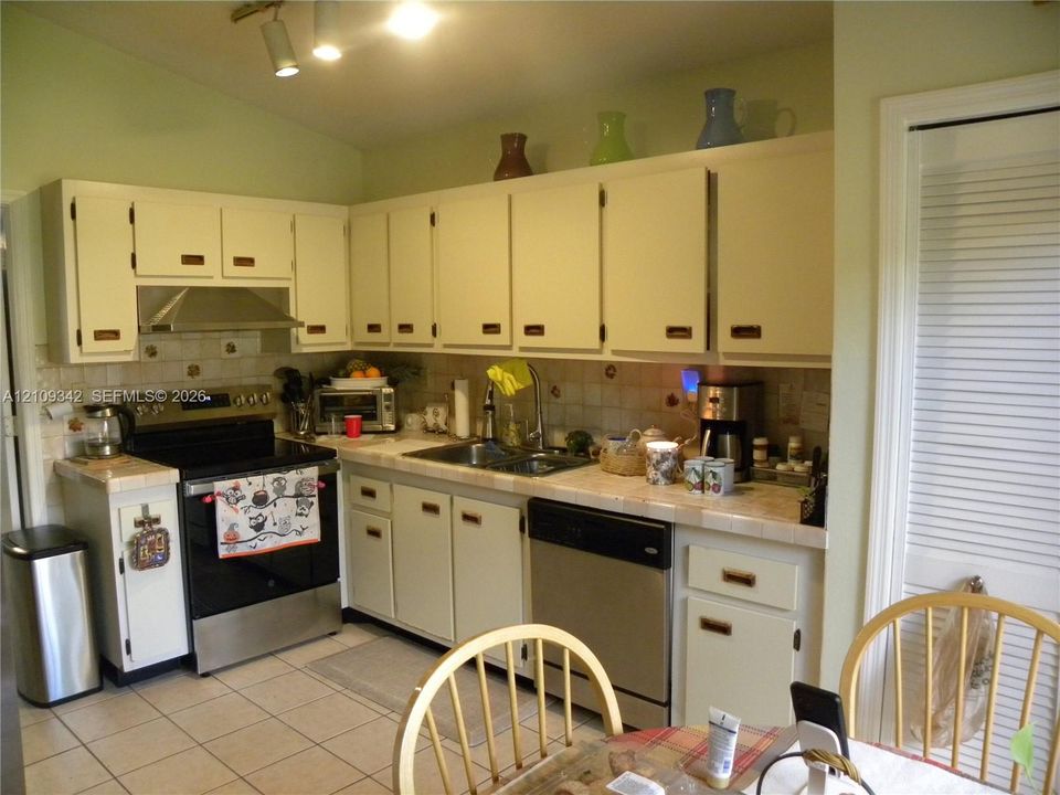 Kitchen featuring white cabinetry, tile countertops, stainless steel appliances, and tile flooring