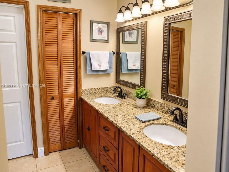 Dual-sink vanity with stone-finish countertop, wood cabinetry, twin framed mirrors, and five-light vanity fixture