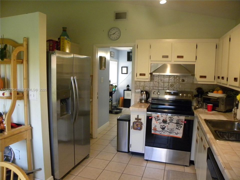 Kitchen featuring white cabinetry, tile countertops, stainless steel side-by-side refrigerator, stainless steel range with integrated hood, and tile flooring