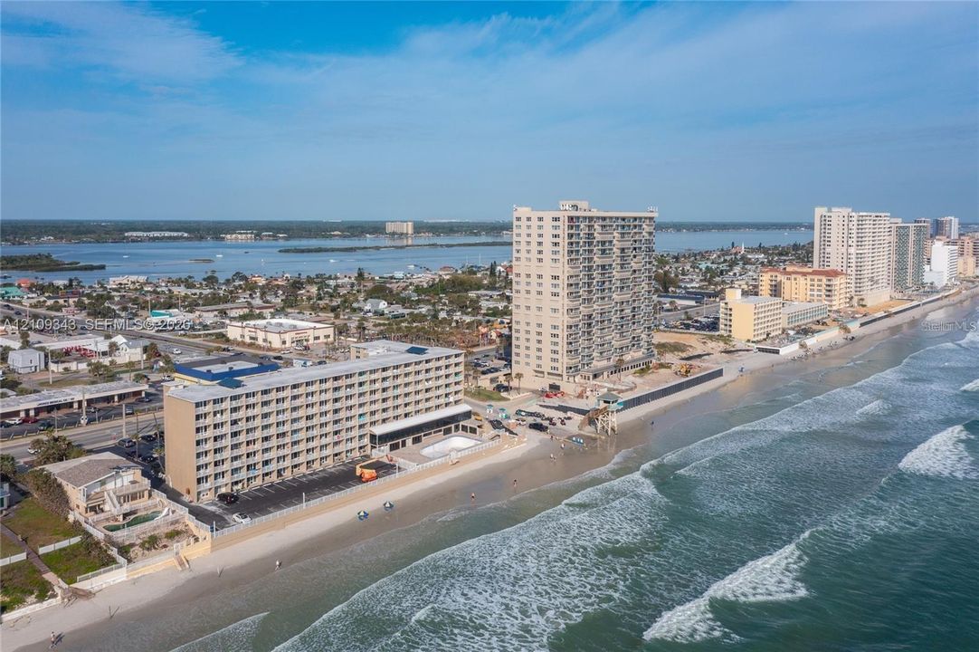Coastal multi-story building featuring direct shoreline access, paved surface parking, and an exterior swimming pool
