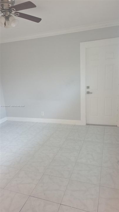 Neutral-toned interior space featuring tile flooring, crown molding, and a multi-paneled door with brushed metal hardware, complemented by an overhead ceiling fan with attached lighting