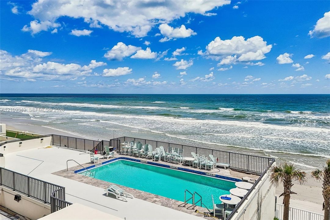 Elevated swimming pool featuring a tile surround, metal perimeter railing, and oceanfront placement