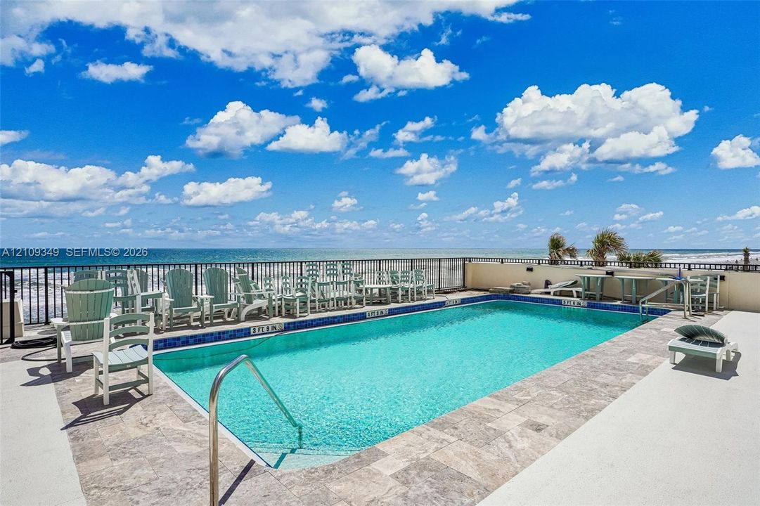 Swimming pool featuring stone-tile coping, metal perimeter fencing, and a metallic handrail