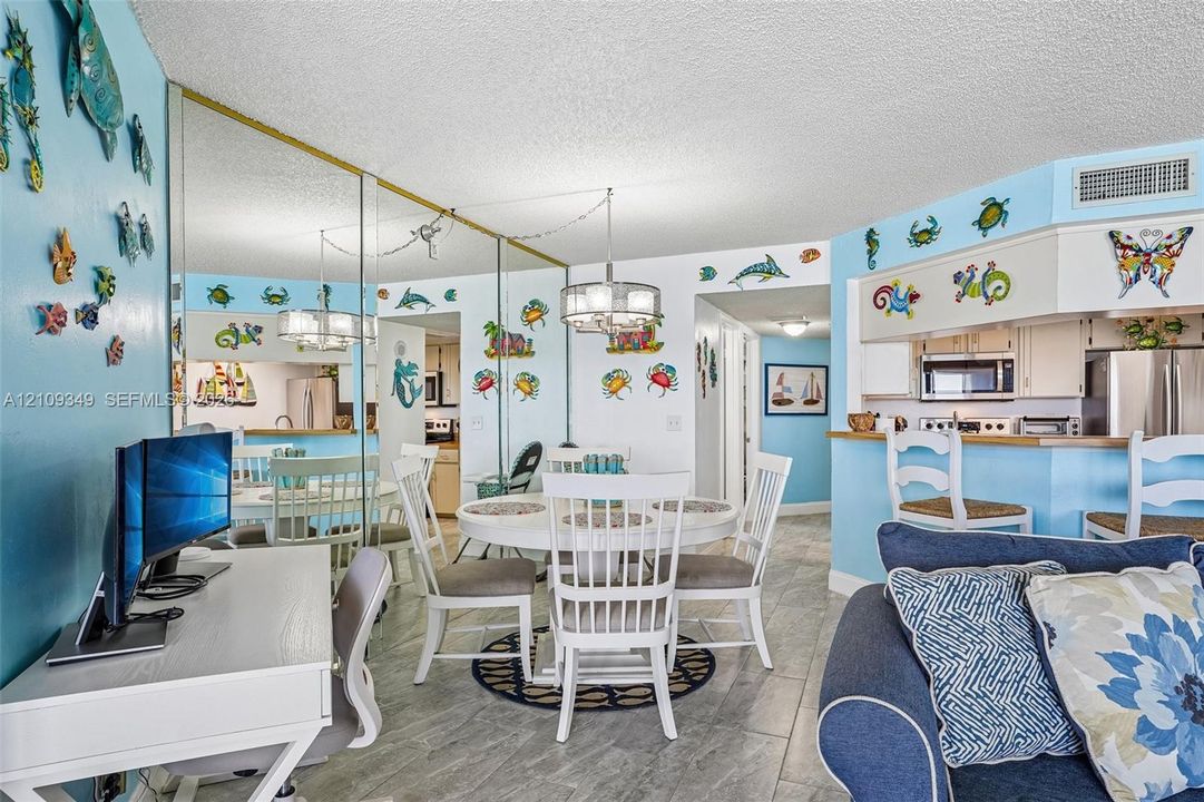 Open-concept dining area featuring oversized wall mirrors, neutral tile flooring, multi-light chandeliers, and a breakfast bar