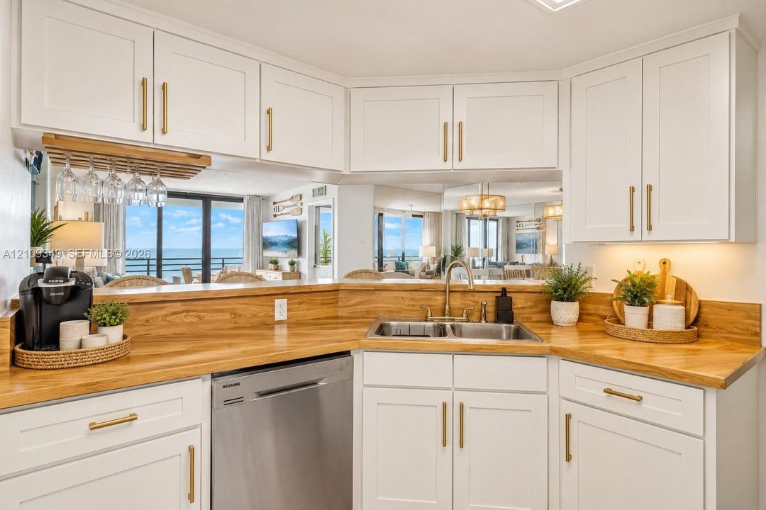 Kitchen featuring white shaker-style cabinetry, wood-finish countertops, brass-toned hardware, a stainless steel dishwasher, and a dual-basin stainless steel sink
