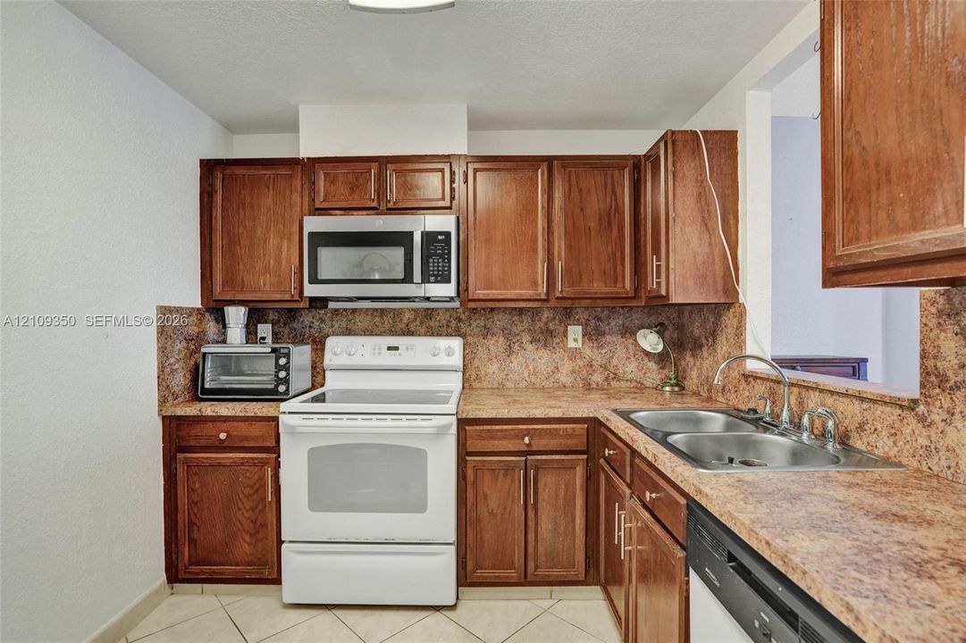 Kitchen featuring stained wood cabinetry, stone-finish countertops, tile flooring, and integrated stainless steel appliances including a range and microwave
