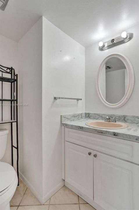 Bathroom vanity featuring a stone-patterned countertop, integrated oval sink, white shaker-style cabinetry, and an oval wall-mounted mirror
