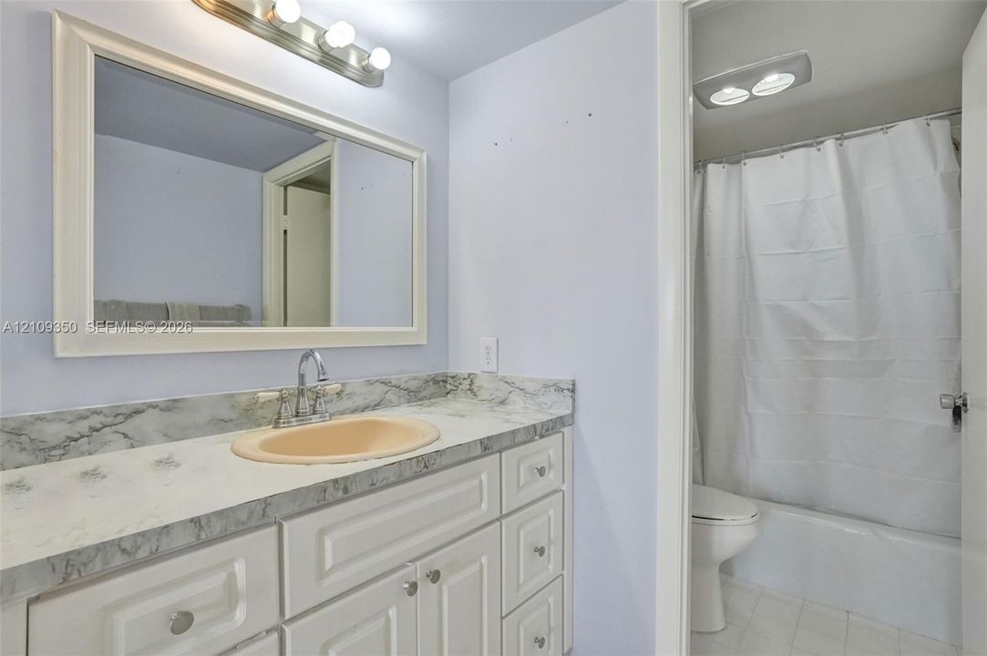 Bathroom featuring a vanity with white cabinetry, a stone-patterned countertop, an oval inset sink, a framed mirror with a four-light fixture, and a tub-shower combination